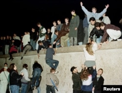 FILE - East German citizens climb the Berlin wall at the Brandenburg Gate as they celebrate the opening of the East German border.