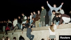 FILE - East German citizens climb the Berlin wall at the Brandenburg Gate as they celebrate the opening of the East German border.