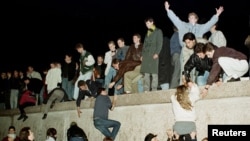 FILE - East German citizens climb the Berlin wall at the Brandenburg Gate as they celebrate the opening of the East German border.