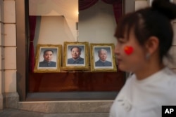 FILE - A woman walks past portraits of late Chinese leaders, including the still-revered Mao Zedong, center, at the Wangfujing Shopping Street in Beijing on April 11, 2024.