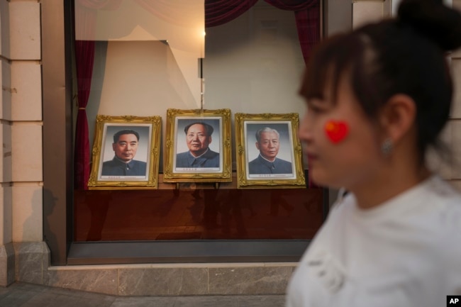 FILE - A woman walks past portraits of late Chinese leaders, including the still-revered Mao Zedong, center, at the Wangfujing Shopping Street in Beijing on April 11, 2024.