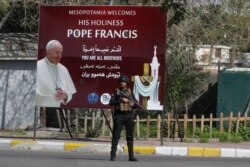 Petugas keamanan berdiri di depan baliho menyambut kedatangan Paus Fransiskus di Baghdad, Irak, 5 Maret 2021.