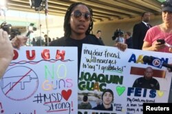 Tyra Hemans, a 19-year-old senior at Marjory Stoneman Douglas High School, sobs as she holds signs honoring slain teachers and friends near the police cordon around the school in Parkland Florida, Feb. 15, 2018.