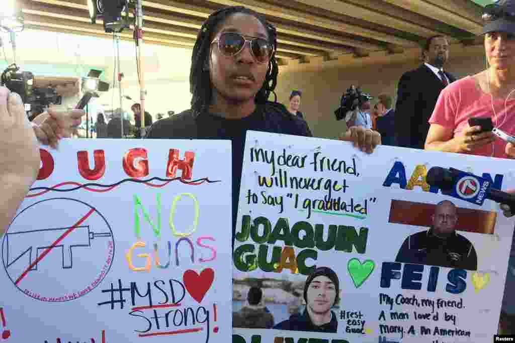 Tyra Hemans, a 19-year-old senior at Marjory Stoneman Douglas High School, sobs as she holds signs honoring slain teachers and friends near the police cordon around the school in Parkland Florida, Feb. 15, 2018.