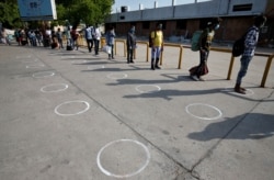 People stand in circles drawn to maintain safe distance while waiting to enter a railway station after a limited reopening of India's rail network in Ahmedabad, India, May 12, 2020.