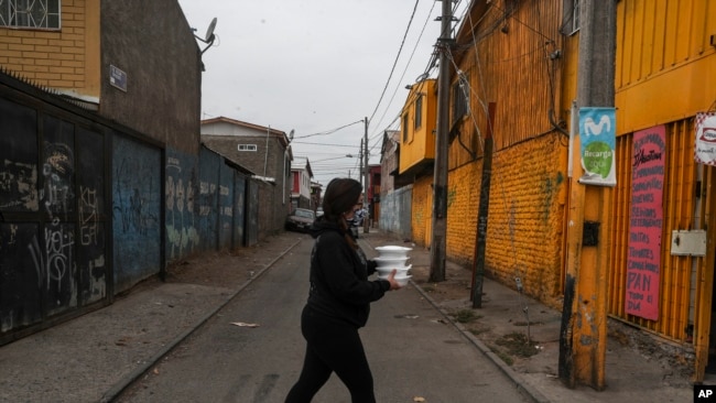 Natalia Sanchez cruza una calle mientras carga con comida para distribuirla entre vecinos que la pasan mal por falta de ingresos durante la pandemia del nuevo coronavirus en El Nocedal a las afueras de Santiago, Chile, el viernes 24 de abril de 2020.