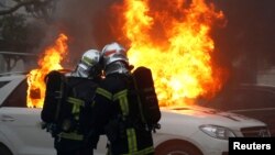 Firefighters try to extinguish flames from a burning car during a demonstration of the yellow vest movement in Nantes, France, Jan. 12, 2019.