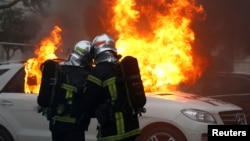 Firefighters try to extinguish flames from a burning car during a demonstration of the yellow vest movement in Nantes, France, Jan. 12, 2019.