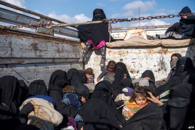 FILE - Women and children fleeing from the last Islamic State pocket in Syria sit in the back of a truck near Baghuz, eastern Syria, Feb. 11, 2019.