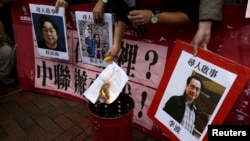 FILE - A pro-democracy activist burns a letter next to pictures of missing staff members of a publishing house and bookstore, including Gui Minhai, owner of Mighty Current, outside the Chinese liaison office in Hong Kong, Jan. 3, 2016.