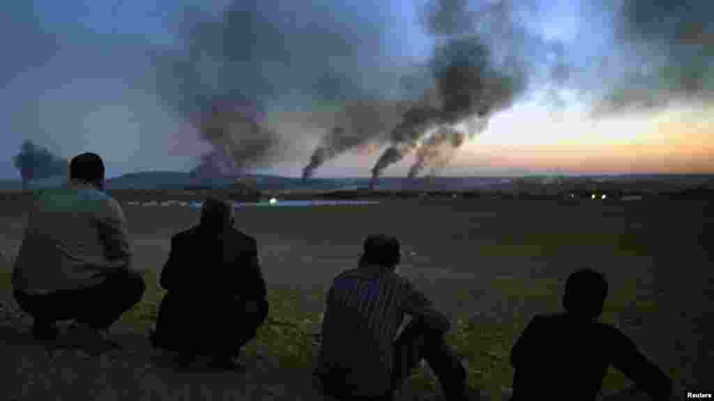 Kurdish refugees watch from a hilltop as thick smoke rises from the Syrian town of Kobani during heavy fighting between Islamic State and Kurdish Peshmerga forces, seen from near the Mursitpinar border crossing on the Turkish-Syrian border, Oct. 26, 2014.