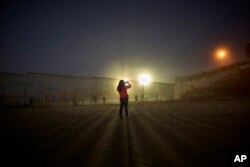 A woman takes a picture as floodlights from the U.S. side light up a border fence, topped with razor wire, Jan. 10, 2019, along the beach in Tijuana, Mexico.