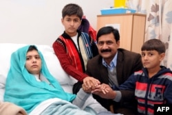 A handout picture received from the Queen Elizabeth Hospital/University Hospitals in Birmingham shows Pakistani schoolgirl Malala Yousafzai sitting on her bed and holding hands with her brothers Khushal Khan (3rd R), Apal Khan (R), and father Ziauddin Yousufzai at the hospital in Birmingham, England, October 25, 2012.