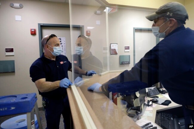 In this Wednesday, May 20, 2020 photo carpenters John Mackie, of Canton, Mass., left, and Doug Hathaway, of Holliston, Mass., right, apply trim to a newly installed plastic barrier in an office area, at Boston University, in Boston. (AP Photo/Steven Senne)