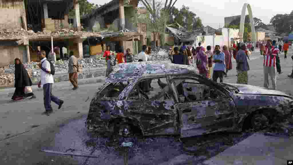 Des passants marchent près d&#39;un&nbsp;bâtiment endommagé et l&#39;épave d&#39;une voiture calciné après le double attentat à Mogadiscio, Somalie, 27 février 2016.