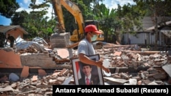A man carries a framed picture of Indonesian President Joko Widodo from a school damaged by an earthquake in Gunungsari, Lombok, Indonesia, Aug. 12, 2018.