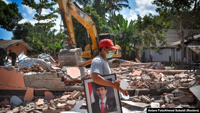 A man carries a framed picture of Indonesian President Joko Widodo from a school damaged by an earthquake in Gunungsari, Lombok, Indonesia, Aug. 12, 2018.