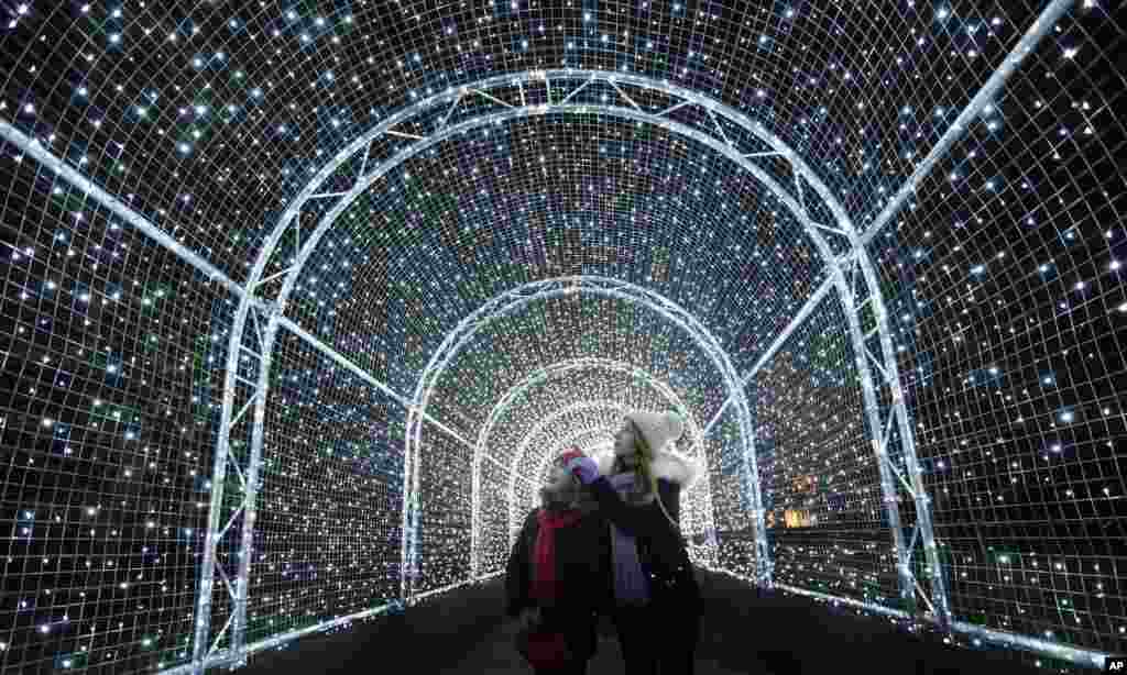 Para pengunjung berjalan di dalam terowongan yang dihiasi cahaya warna-warni, bagian dari perayaan Natal di Kew Gardens, London, Inggris.