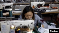 FILE - A woman works in a small-sized factory producing clothes and hats, in which more than half of its production line has stopped its operation because of a downturn in its business at the Qingyundian industrial zone in Beijing.