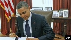 President Barack Obama signs the payroll tax cut extension in the White House Oval Office, in Washington, December 23, 2011.