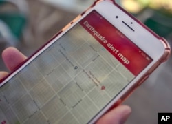 A mobile phone customer looks at an earthquake warning application on their phone in Los Angeles, Jan. 3, 2019. Los Angeles has released the app that could give county residents precious seconds to drop, cover and hold on in the event of a quake.