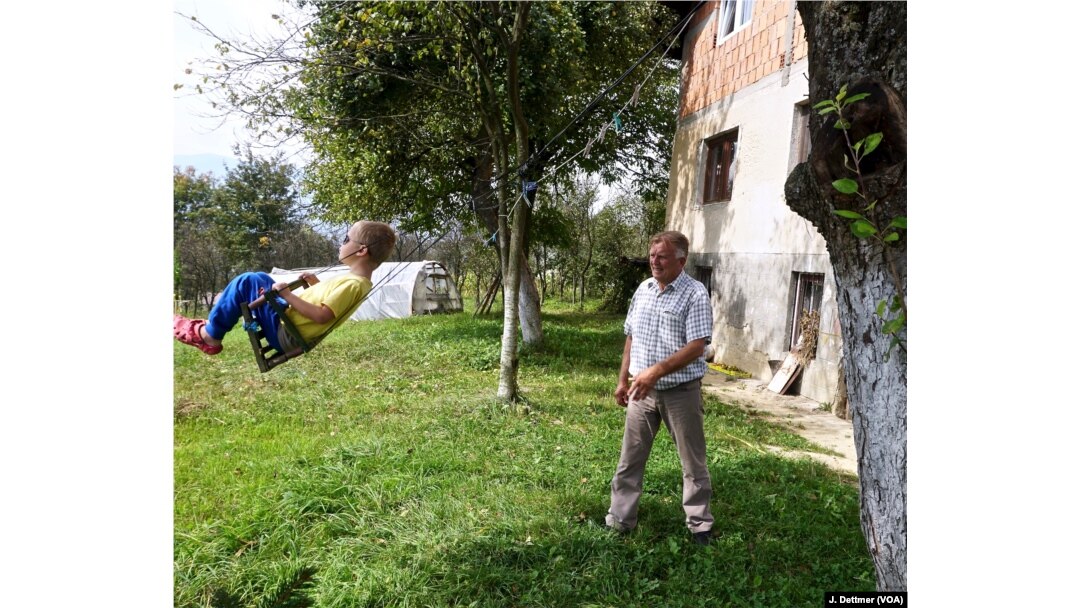 Huso Ahmić, now 72 years old, plays with a grandson in the garden of his family home, which was rebuilt after it was razed in the 1993 attack. His parents died in the blaze.
