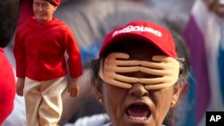 Una mujer simpatizante del presidente Nicolás Maduro, usa un juego de manos sobre su cara y un muñeco de Hugo Chávez durante un evento de campaña.