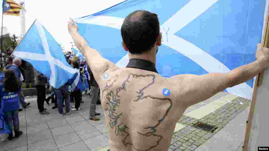 Seorang pendukung pemisahan Skotlandia dengan tato wilayah tersebut di punggungnya memegang bendera Saltire di luar kantor BBC di Glasgow, Skotlandia (14/9).&nbsp;(Reuters/Paul Hackett)