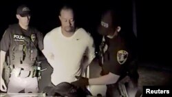 Tiger Woods is seen handcuffed and searched by police officers in this still image from police dashcam video in Jupiter, Florida, May 29, 2017.