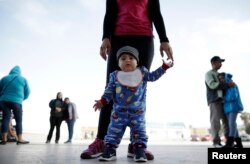 Nine month-old Jesus Alberto Lopez, center, stands with his mother, Perla Murillo, as they wait with other families to request political asylum in the United States, across the border in Tijuana, Mexico.