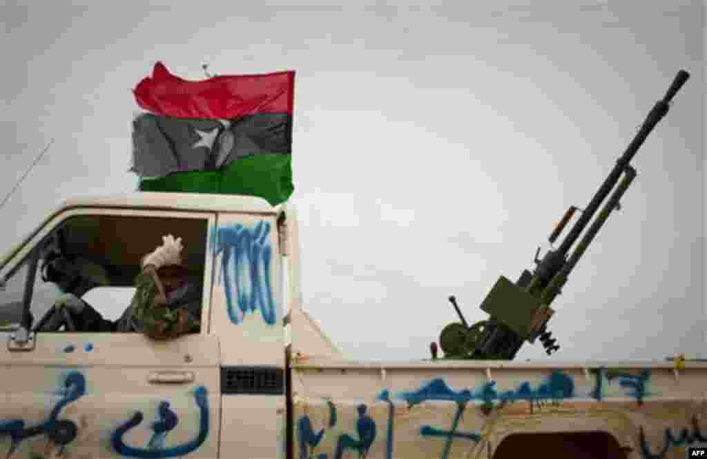 A Libyan rebel gestures as he arrives with heavy weapon on top of his truck to the frontline near Sultan, south of Benghazi, Libya, Friday, March 18, 2011. The U.N. Security Council voted Thursday to impose a no-fly zone over Libya and authorize "all nec