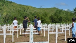 Boys play among the crosses that mark the 3,000 buried in the mass grave at the Holy Cross Memorial Park. The dead here are not identified, but people wrote the names of their lost loved ones on the white crosses, Tacloban City, Philippines, Nov. 8, 2014. (Simone Orendain/VOA)