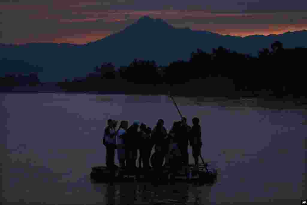 Central American migrants stand on a raft to cross the Suchiate River from Guatemala to Mexico, as the Tacana volcano stands tall near Ciudad Hidalgo, Mexico.