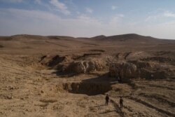 In this Nov. 11, 2017 photo, two Iraqi men walk near a sinkhole known as Khasfa, that is believed to contain the remains of thousands of people executed by Islamic State militants near Adhbah, south of Mosul, Iraq.