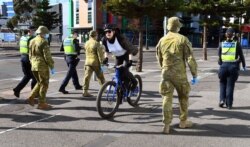 A cyclist passes a group of police and soldiers patrolling the Docklands area of Melbourne on Aug. 2, 2020, after the announcement of new restrictions to curb the spread of the COVID-19 coronavirus.