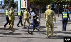 A cyclist passes a group of police and soldiers patrolling the Docklands area of Melbourne on Aug. 2, 2020, after the announcement of new restrictions to curb the spread of the COVID-19 coronavirus.