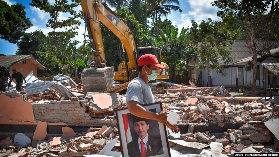 Seorang pria membawa foto Presiden Joko Widodo dari sekolah yang rusak akibat gempa di Gunungsari, Lombok, 12 Agustus 2018.