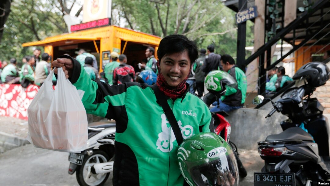 Pengemudi Go-Jek menunjukkan bungkusan makanan yang dipesan oleh pelanggannya di depan sebuah kios makanan, di Jakarta, Indonesia, 13 Juli 2017.