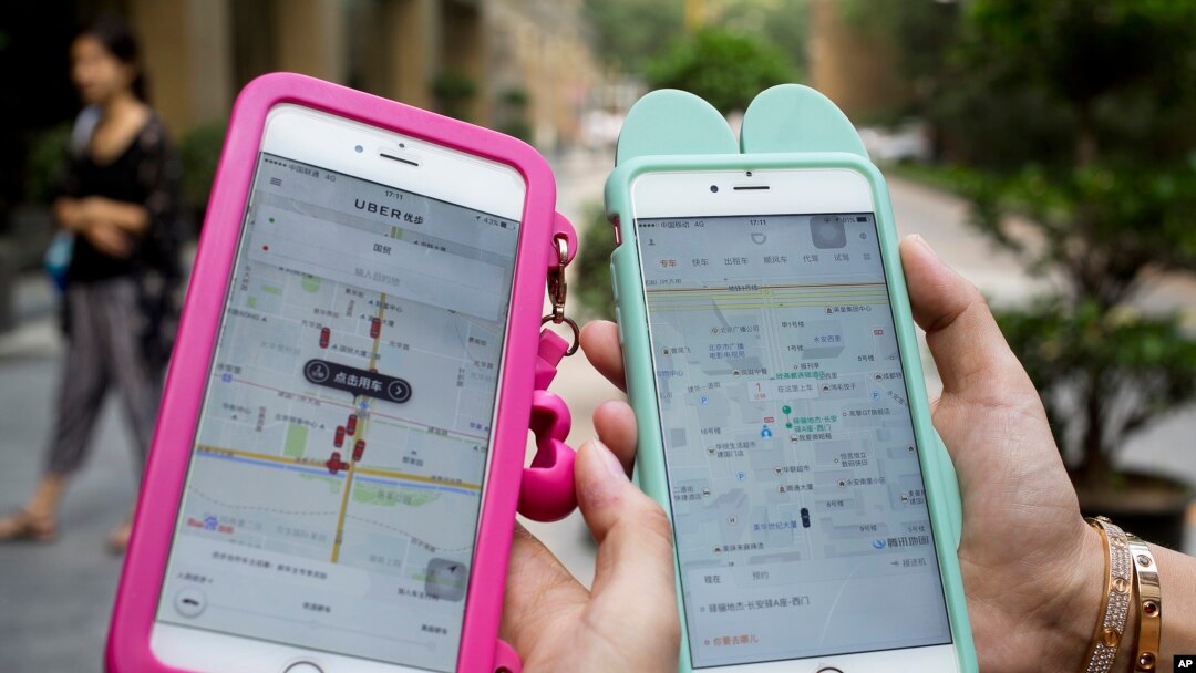 Women holding their smartphones show the ride-hailing apps Uber Technology Ltd., left, and Didi Chuxing at a residential compound in Beijing, Aug. 1, 2016. 
