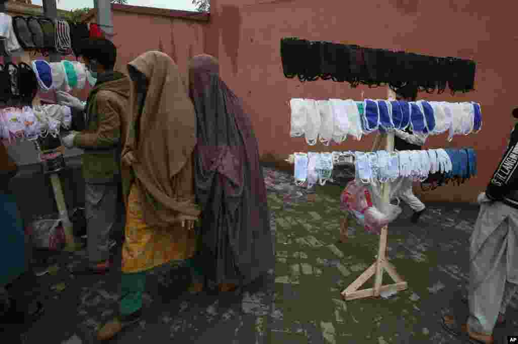 Pakistani women walk past vendors selling face masks to prevent the spread of the coronavirus, in Peshawar.