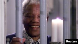 Cố Tổng thống Nam Phi Mandela cầm cây nến biểu tượng thiên niên kỷ, đứng sau song sắt nhà tù ở Robben Island, nơi ông bị giam giữ. (Ảnh tư liệu, 31/121999).
