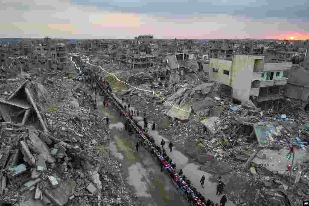 As the sun sets, Palestinians sit at a large table surrounded by the rubble of destroyed homes and buildings as they gather for iftar, the fast-breaking meal, on the first day of Ramadan in Rafah, southern Gaza Strip, March 1, 2025