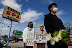 FILE - People hold placards during a vigil at a makeshift memorial outside the Gold Spa following the deadly shootings in Atlanta, Georgia, March 21, 2021.