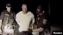 FILE - Tiger Woods is seen handcuffed and searched by police officers in this still image from police dashcam video in Jupiter, Florida, May 29, 2017.