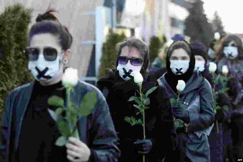 Women in black clothing with their mouths sealed with a tape walk down the street with white roses in Minsk as they protest against the verdict against the Belarusian journalist and doctor who were sentenced to jail.