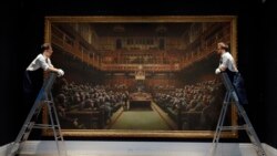 Sotheby's employees look at a painting by anonymous street artist Banksy on display at Sotheby's auction rooms in London.