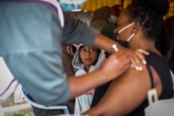 A Kenyan woman receives a dose of coronavirus vaccine donated by Britain, as her son watches, at the Makongeni Estate in Nairobi, Kenya Aug. 14, 2021.