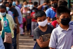 FILE - Children and adults wait in lines for donated food at a makeshift camp for migrants near the U.S.-Mexico border, May 14, 2021, in Reynosa, Mexico.