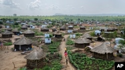 Des femmes et des enfants rentrent chez eux avec des récipients en plastique d'eau au milieu de maisons en briques de boue et de tentes dans le camp de réfugiés Bidi Bidi, dans le nord de l'Ouganda, 9 juin 2017.