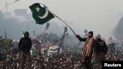 A supporter of Tahir-ul Qadri waves a Pakistani flag as he walks on a container on the third day of protests in Islamabad, Pakistan, January 16, 2013.